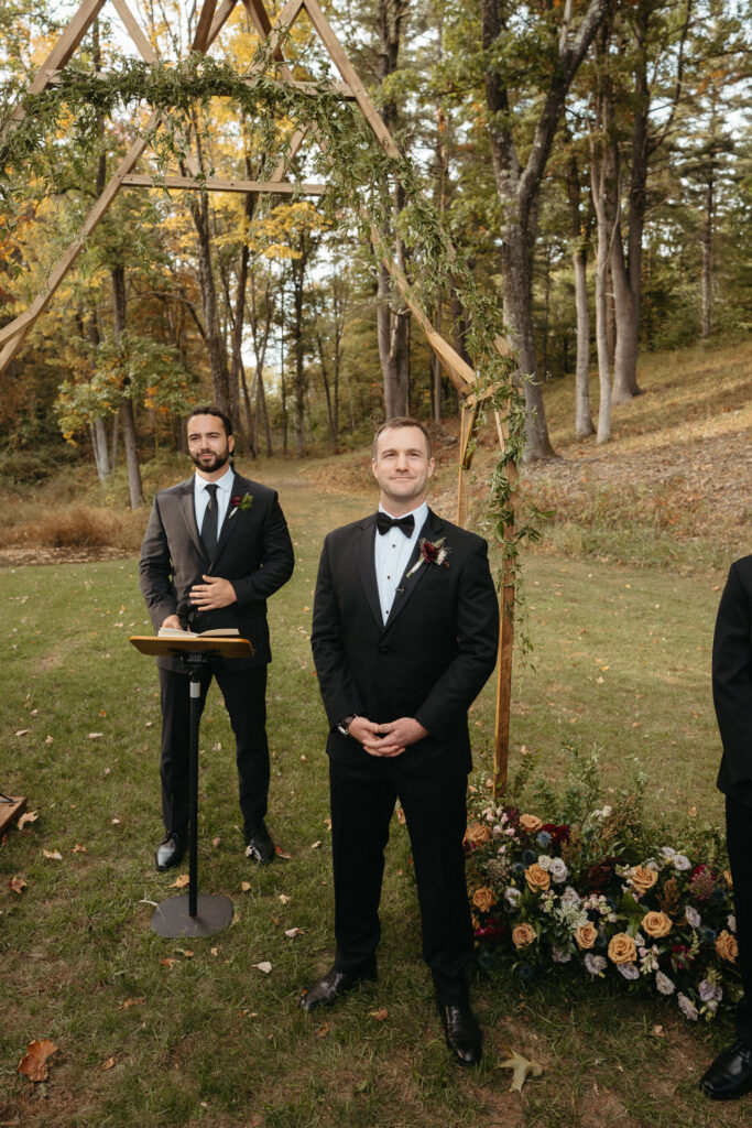 Two people in tuxedos waiting at the ceremony arch