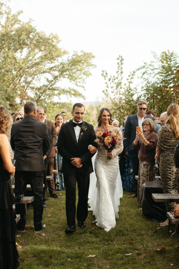 Person in a gown walking down the aisle on an escort's arm, holding a bouquet