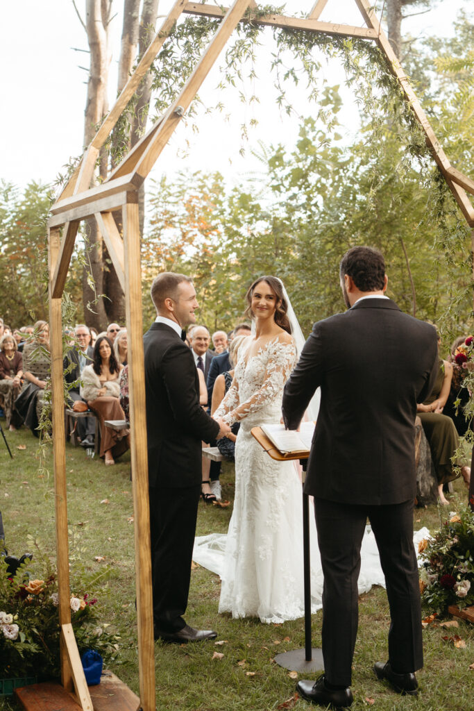 Couple holding hands under a wooden arch with the officiant