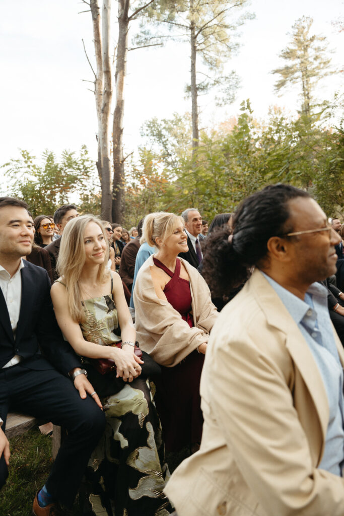 Guests smiling during the ceremony, one in a beige jacket
