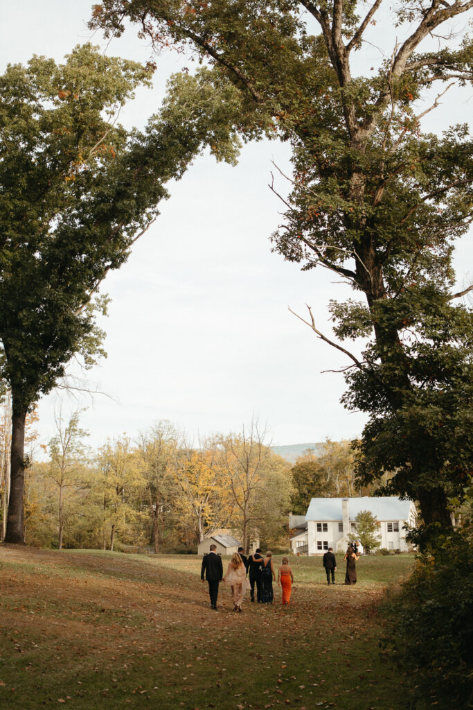 Wedding party walking across a field toward the farmhouse in the distance
