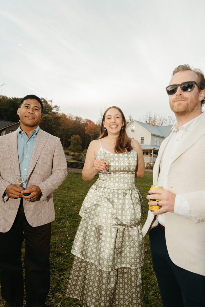 Three guests smiling on the lawn with the farmhouse behind them