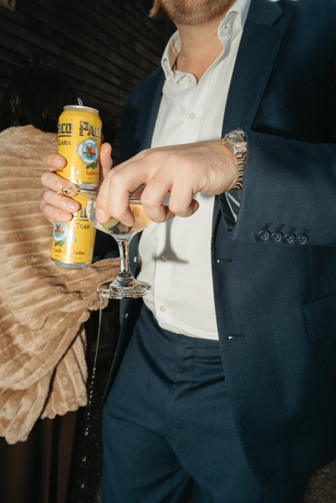 Guest in a navy suit holding a beer can and a glass