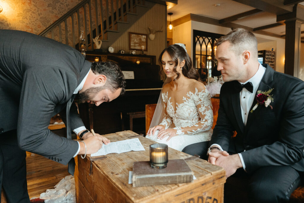 Couple signing the marriage license at a wooden table in the farmhouse