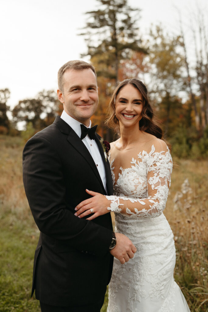 Couple smiling together in a field, one with an arm around the other