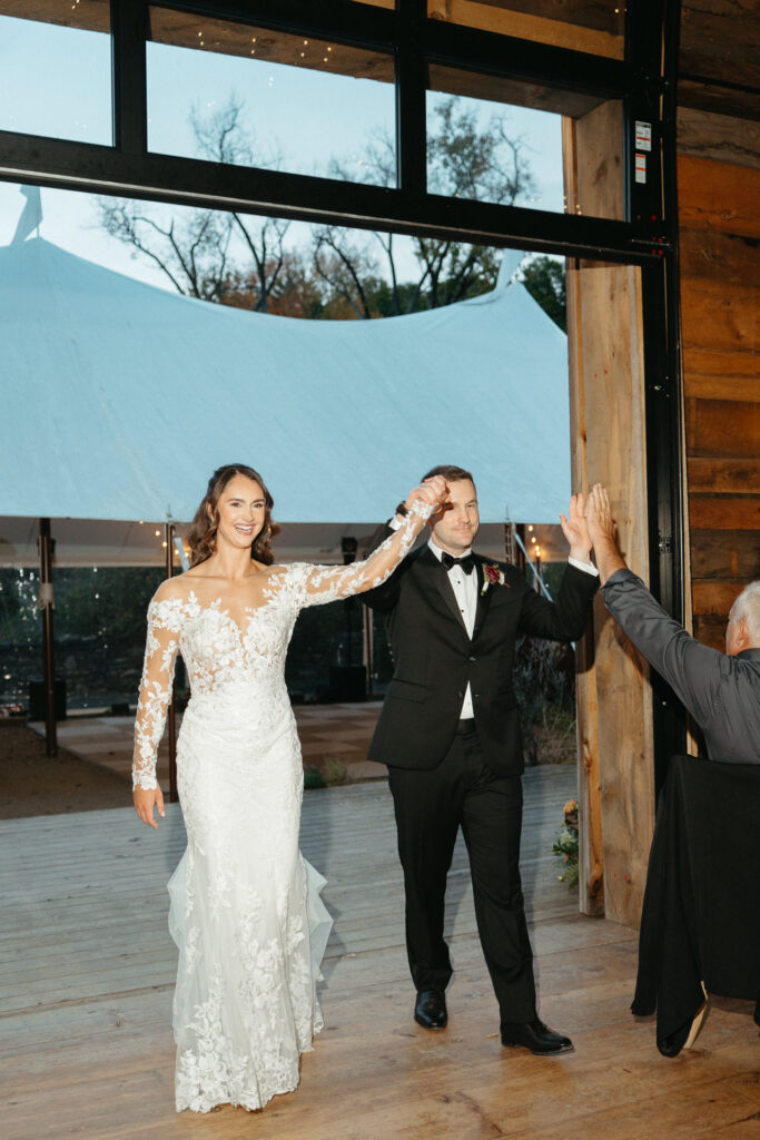 Couple entering the barn reception, one with a hand raised