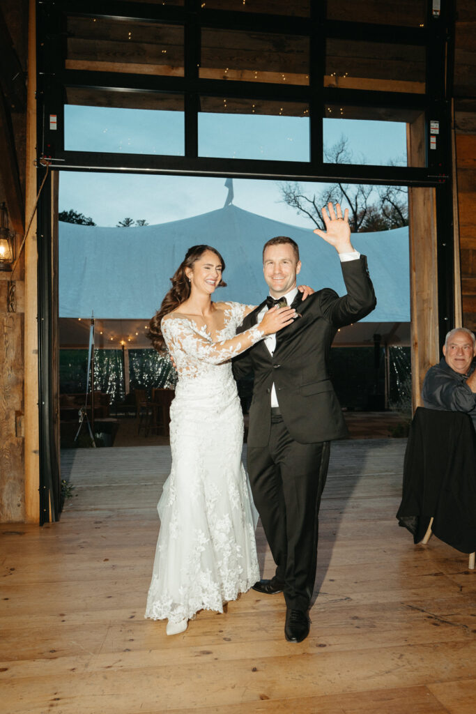 Couple waving to guests with arms raised in the barn