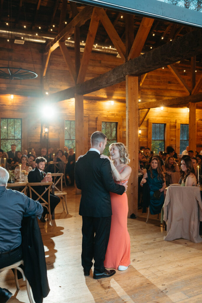 Person in a tuxedo dancing with a guest in a coral dress as guests watch