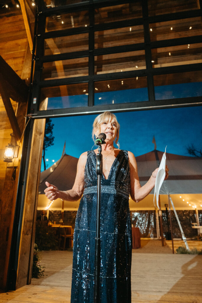 Guest in a beaded blue gown giving a toast at a microphone