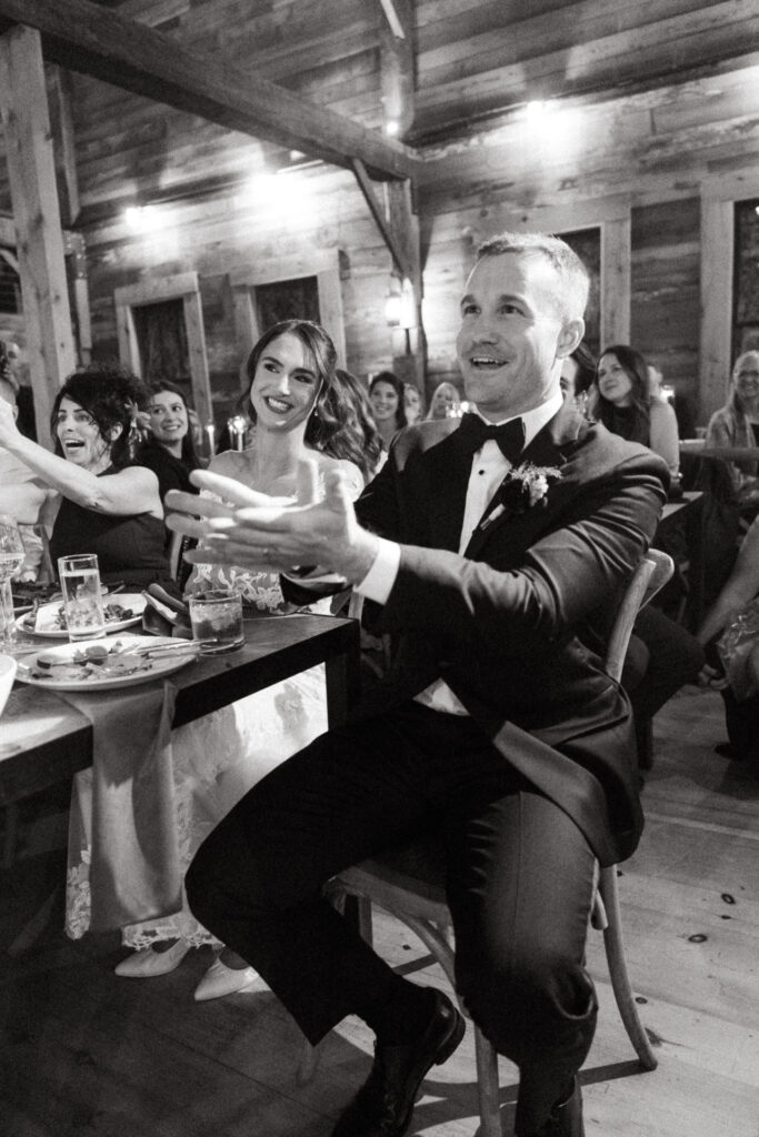 Black and white photo of a person in a tuxedo reaching out, laughing at the table
