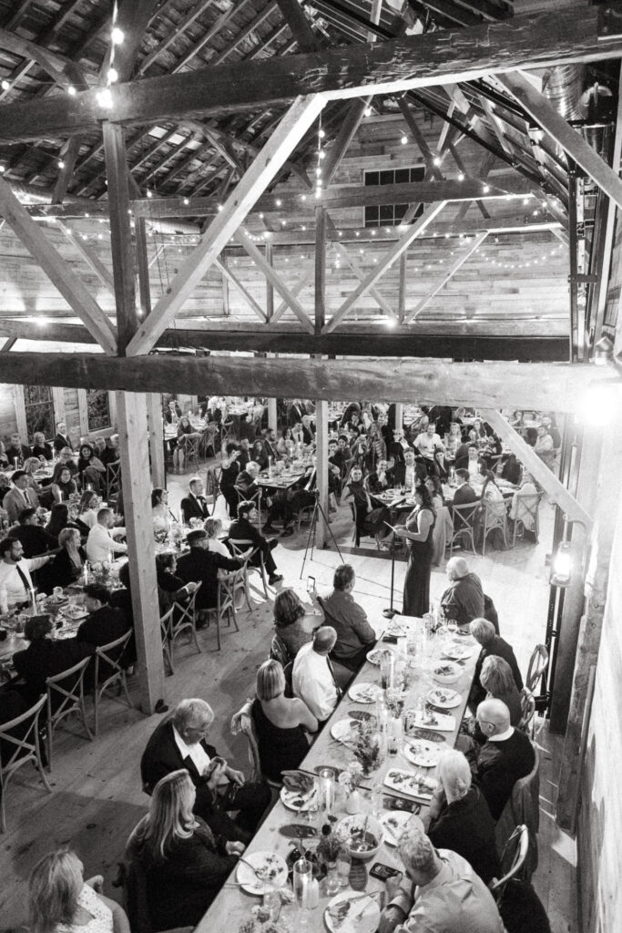 Black and white view of the barn rafters and guests at long tables