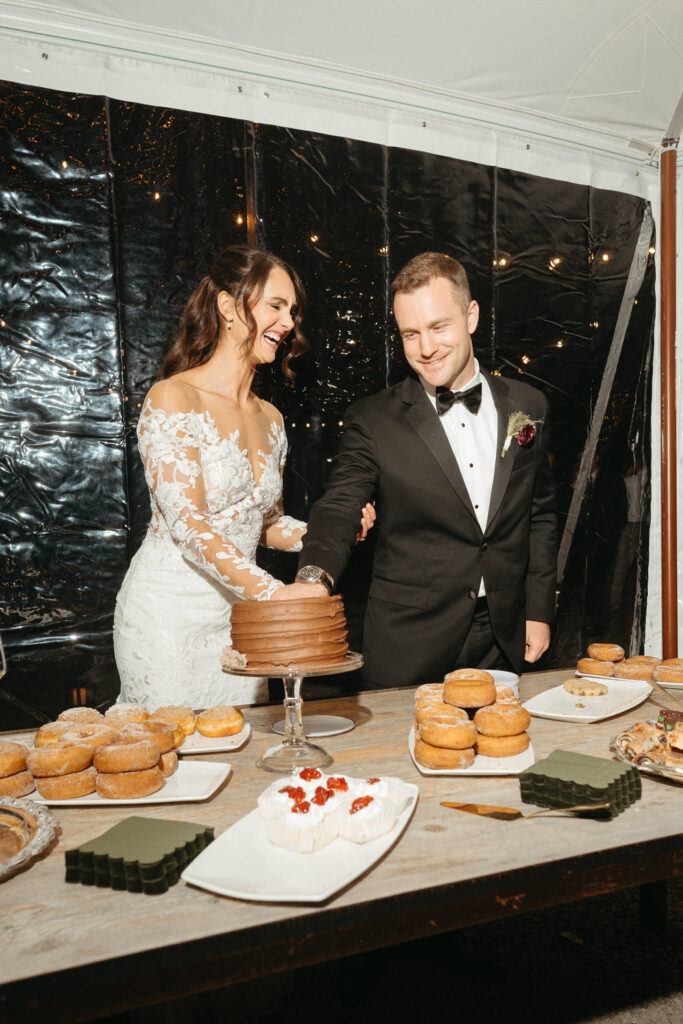 Couple cutting a chocolate cake on a dessert table with doughnuts