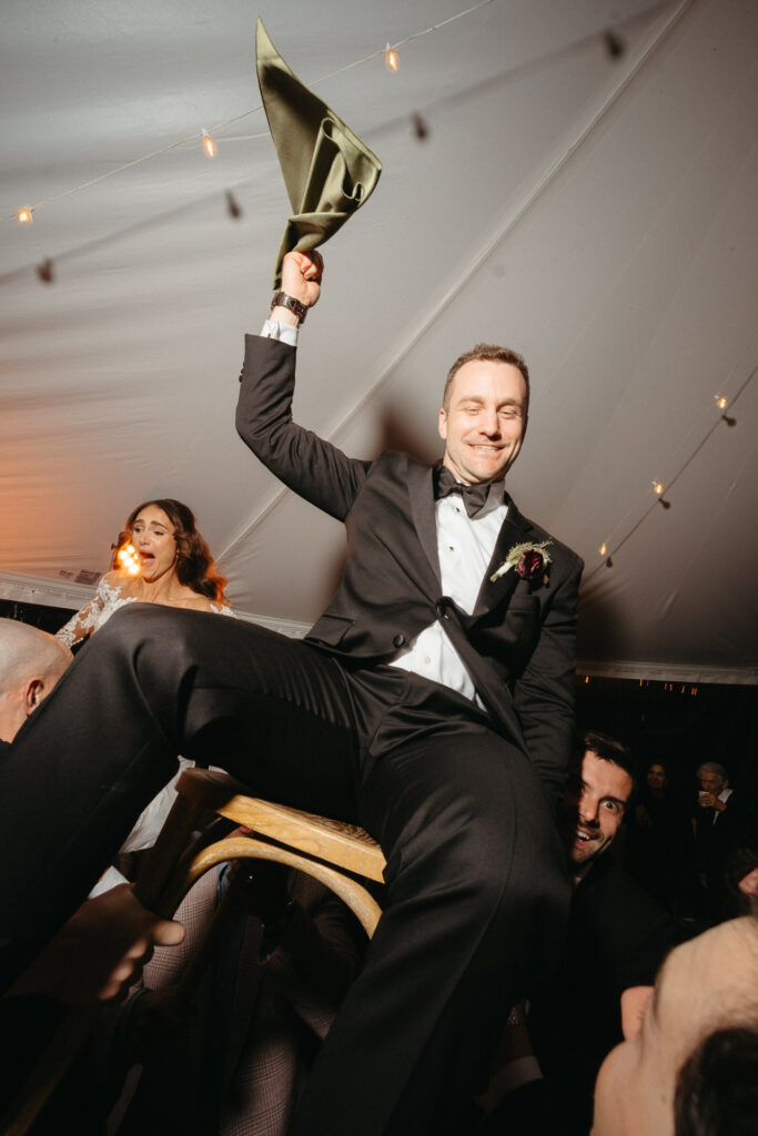 Person in a tuxedo lifted on a chair above the dance floor