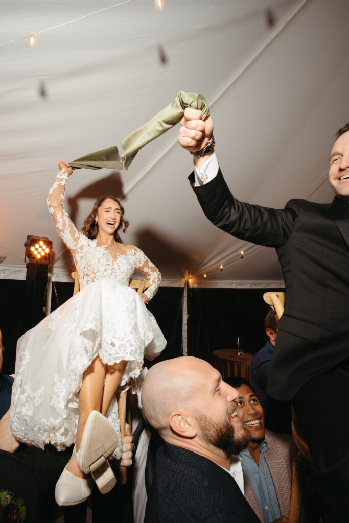 Person in a gown lifted on a chair, holding a napkin overhead
