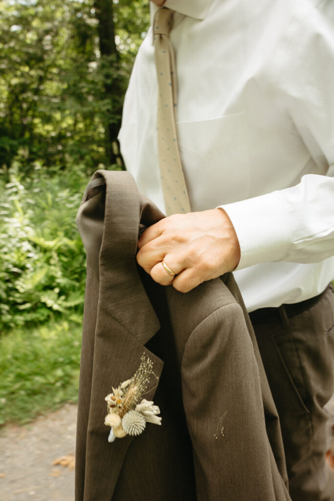 Hand holding a suit jacket with a small boutonniere pinned to it