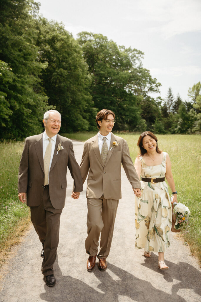 Person in a taupe suit walking arm in arm between two guests on the path