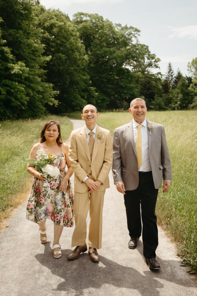 Person in a tan suit walking between two guests, one in a floral dress and one in a gray suit