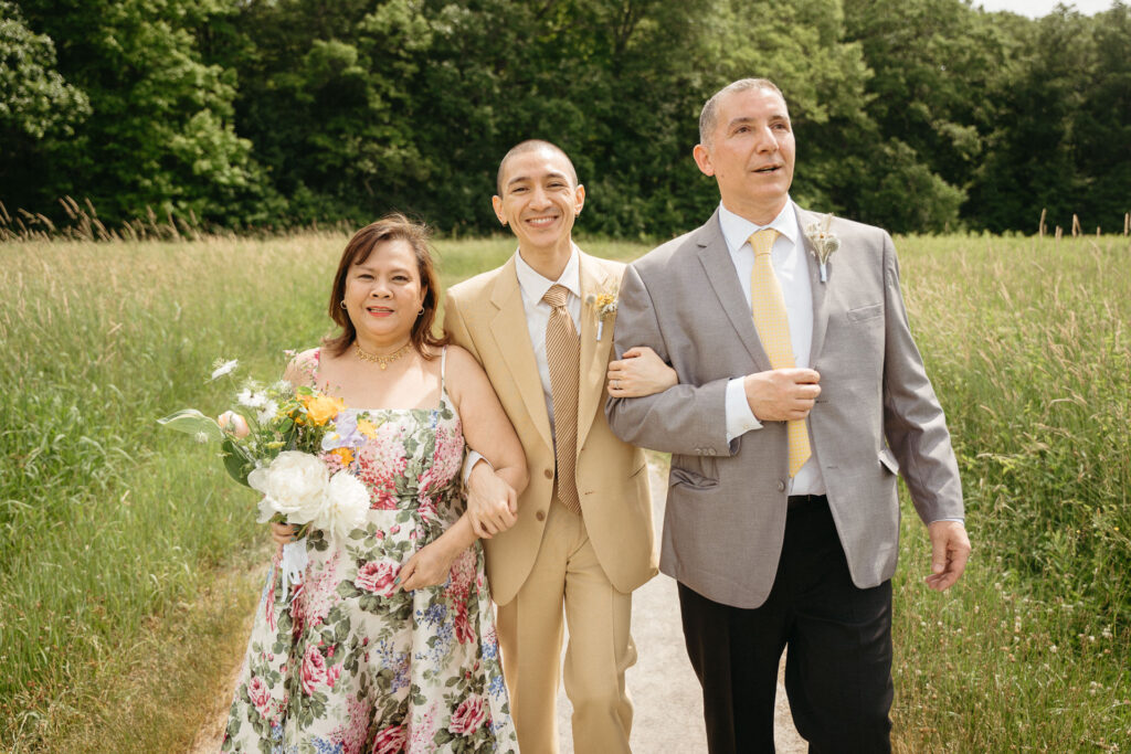 Person in a tan suit walking arm in arm with a guest in a floral dress and a guest in a gray suit