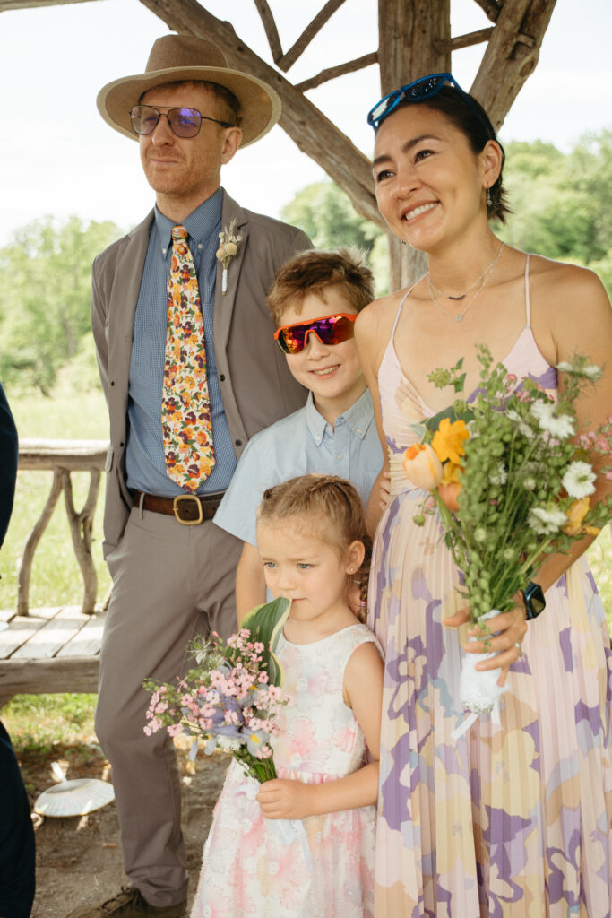 Guest in a hat and a guest in a pastel dress holding wildflowers, with two children