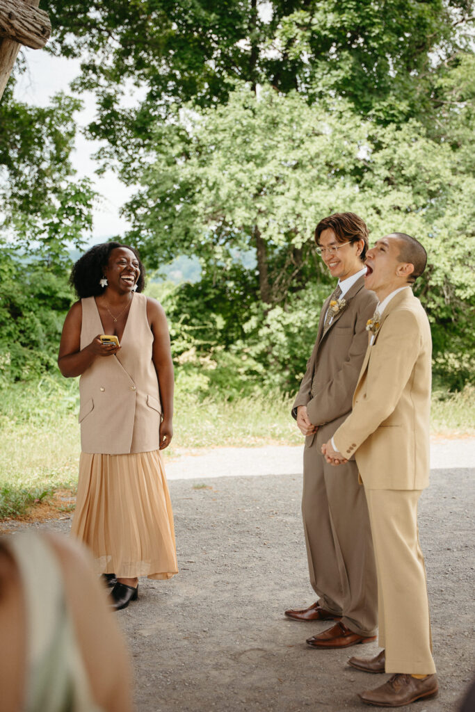 Guest in a tan vest laughing as the couple listens