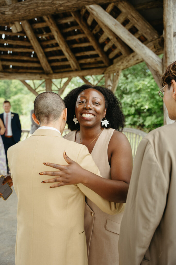 Guest in a tan vest hugging the person in a tan suit, beaming