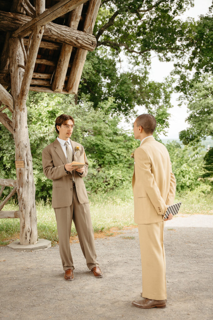 Person in a taupe suit reading from a paper under the gazebo as the person in a tan suit listens