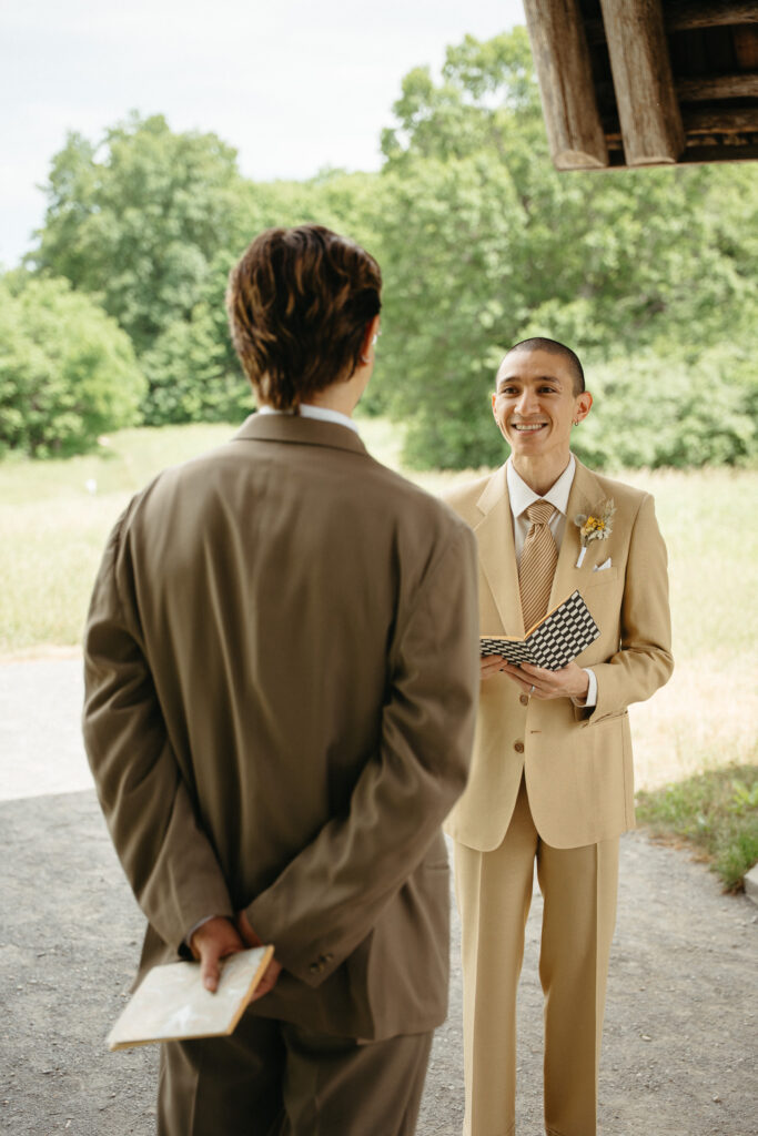 Person in a taupe suit standing with hands behind their back as the person in a tan suit smiles