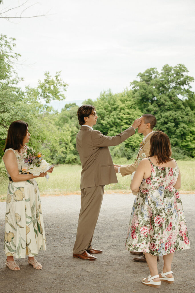 Couple exchanging rings in front of the field with two guests holding bouquets