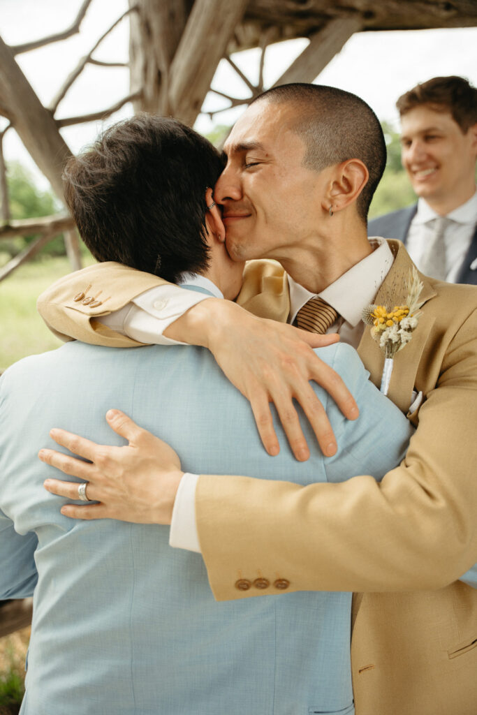 Person in a tan suit hugging a guest in a light blue suit