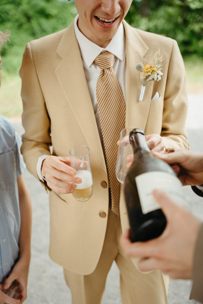 Person in a tan suit laughing as sparkling wine is poured into a glass