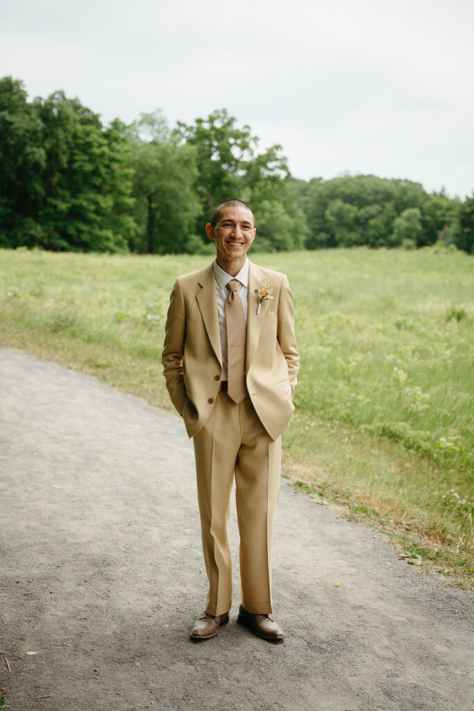 Person in a tan suit standing on a gravel path with the meadow behind